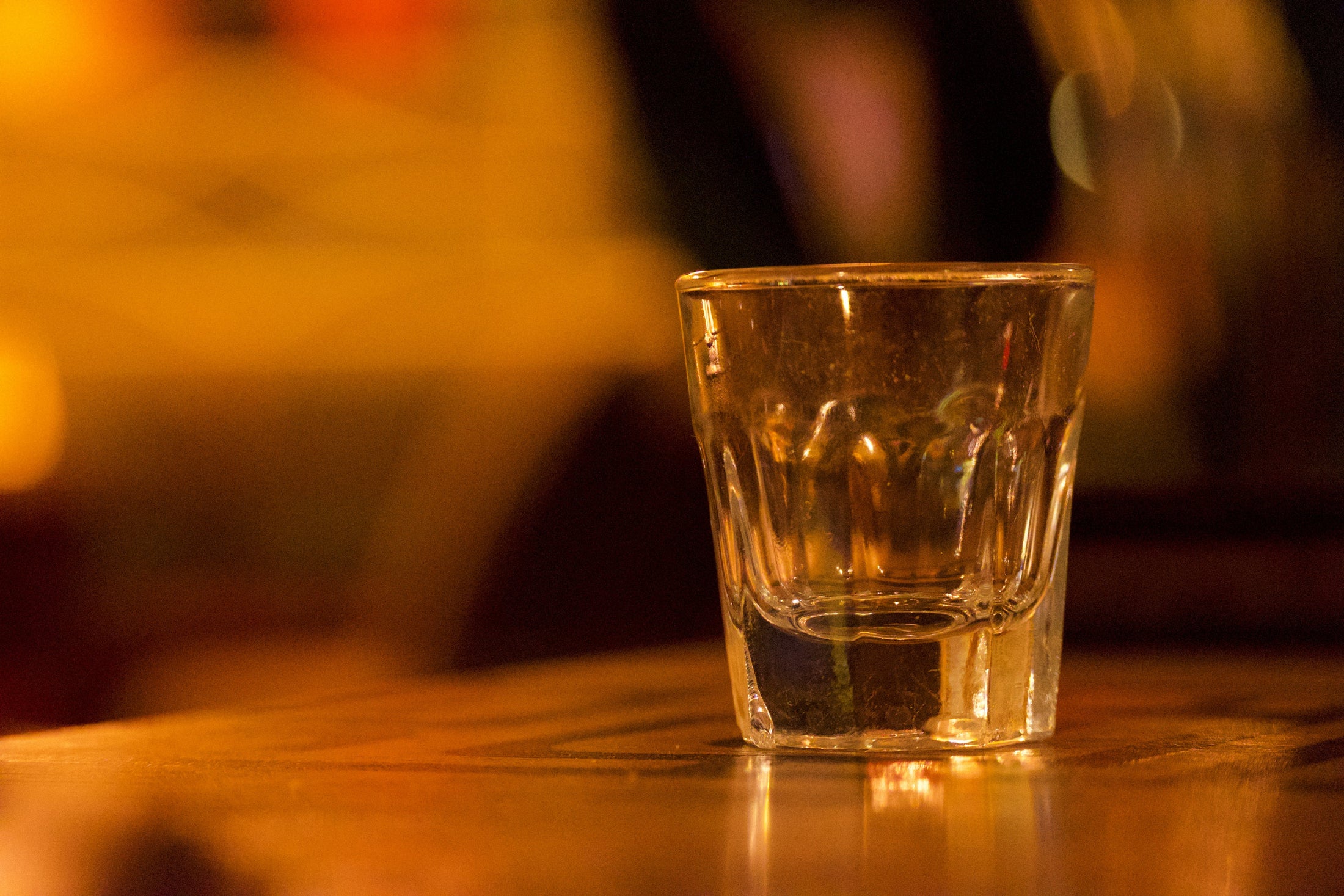 Clear shot glass filled with whiskey on a wooden bar counter, shot glass size guide