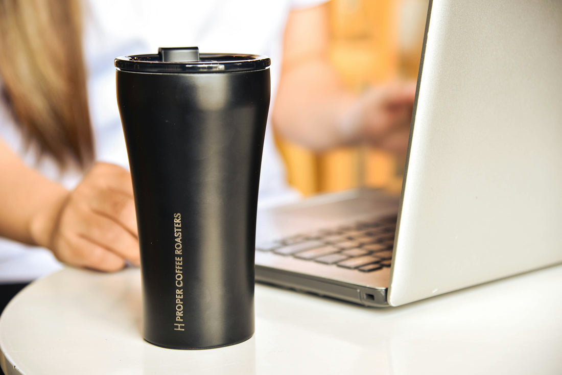 Black insulated travel tumbler on a desk next to a laptop, an everyday tumbler idea for Photo USA wholesale sublimation tumbler blanks