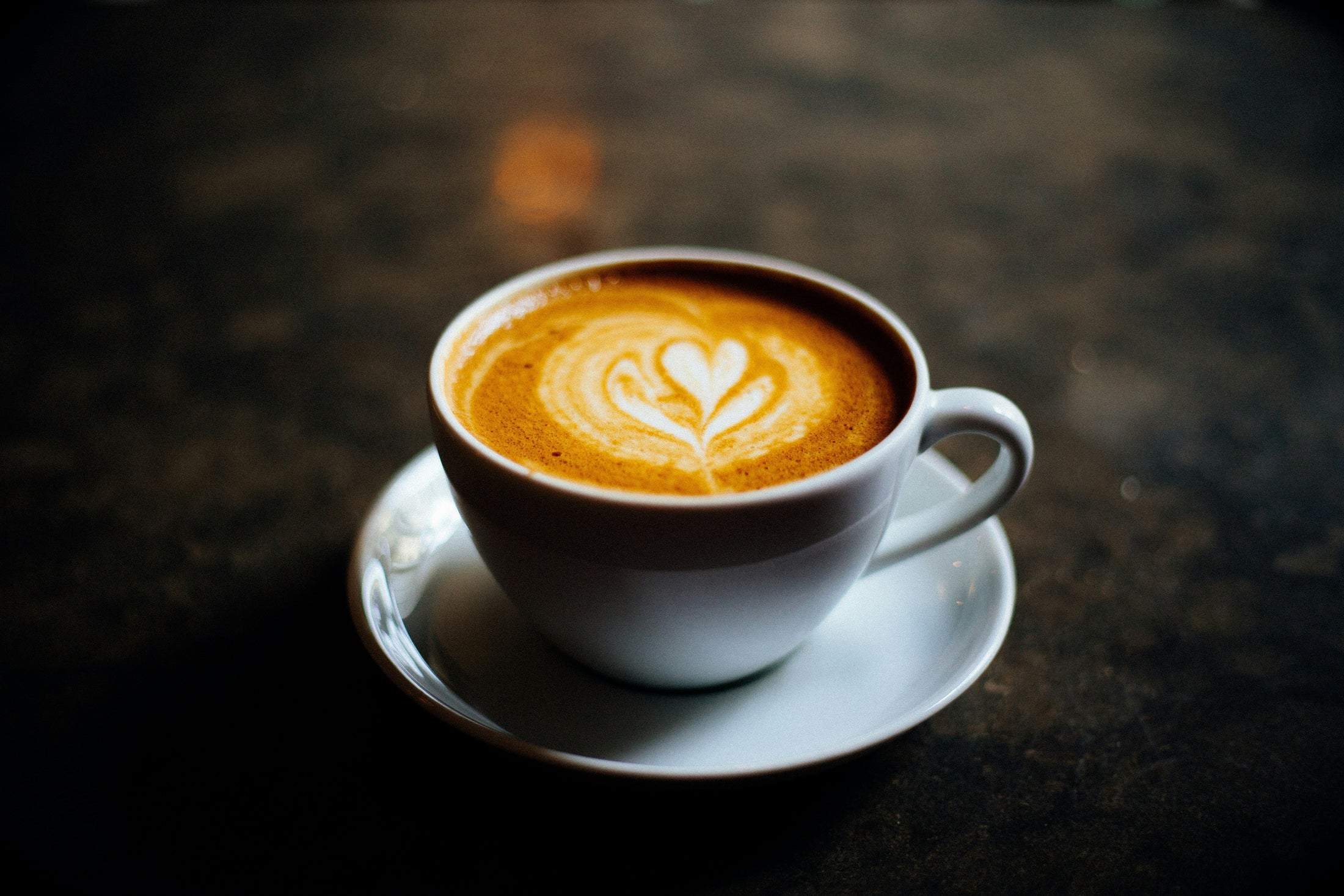 White ceramic coffee cup with latte art on a saucer, representing wholesale ceramic coffee mug blanks sold by the case