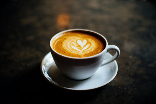 White ceramic coffee cup with latte art on a saucer, representing wholesale ceramic coffee mug blanks sold by the case