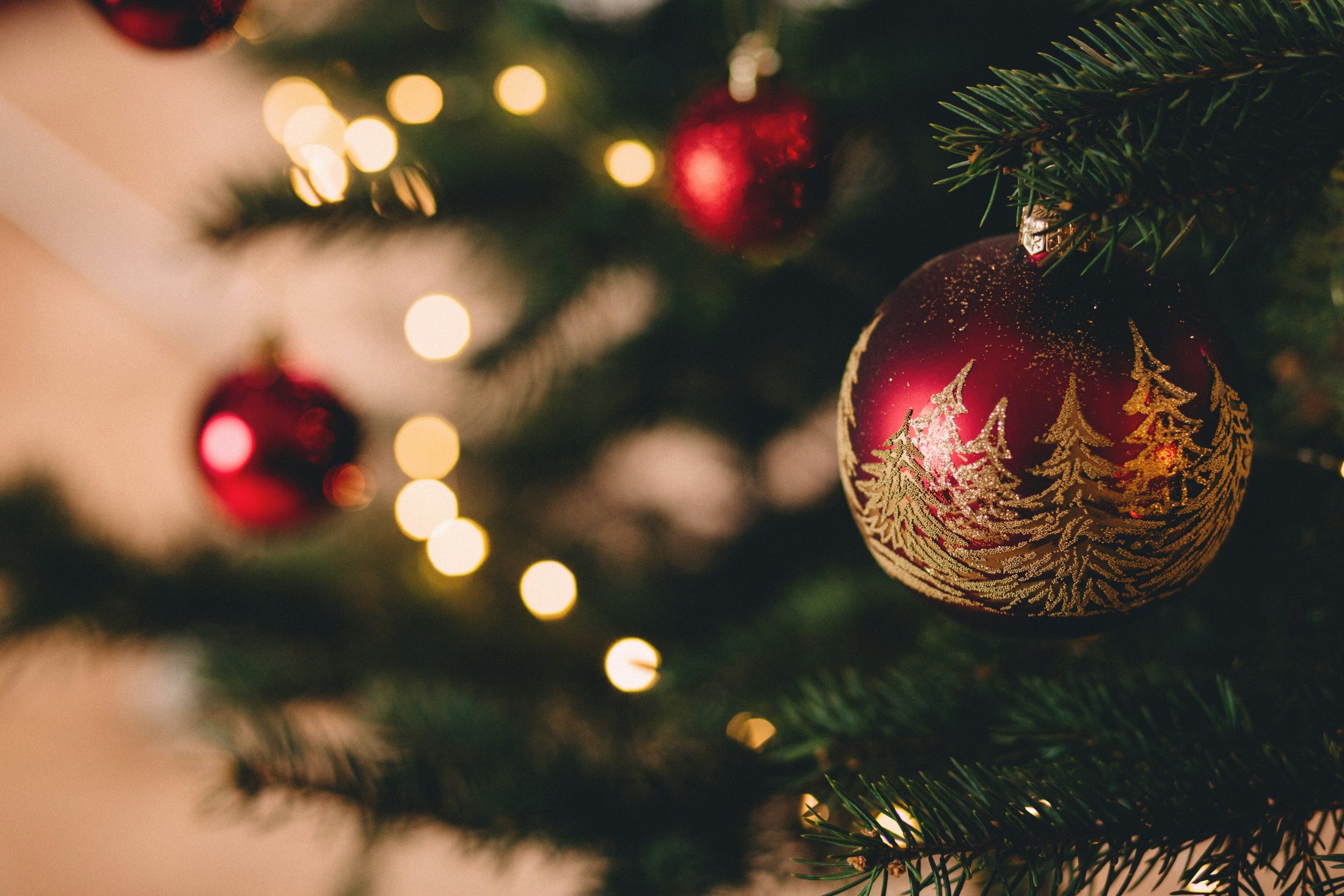 Red Christmas ornament with gold tree pattern hanging on a lit Christmas tree, Christmas mug and ornament gift guide