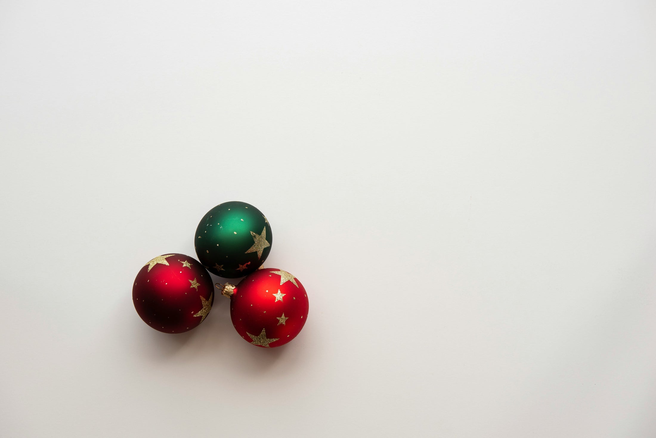 Three red and green Christmas ball ornaments with gold stars on a white background, representing photo ornament ideas for wholesale sublimation ornament blanks