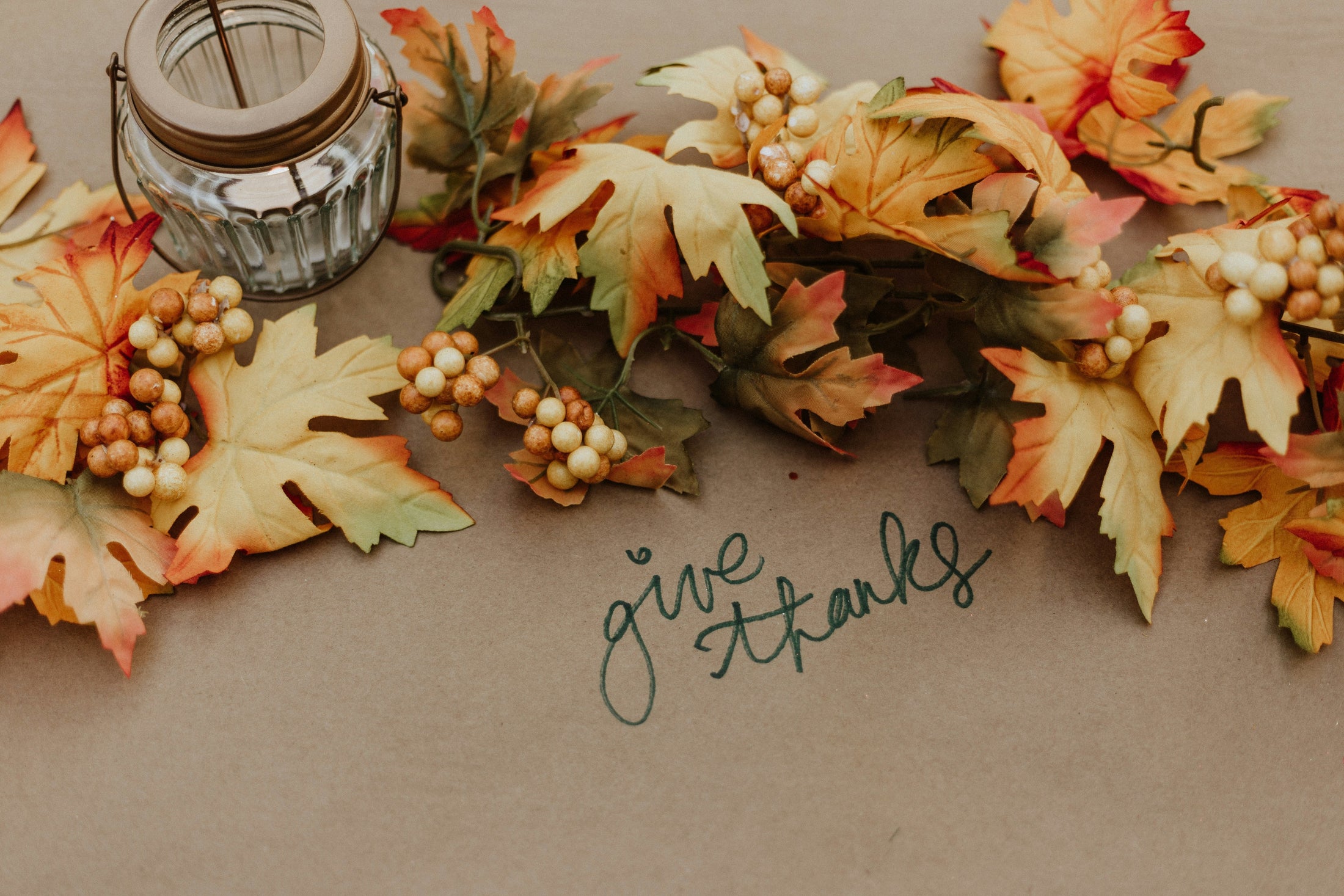 Autumn maple leaves and berries with a glass lantern and handwritten "give thanks" on kraft paper, Thanksgiving host gift guide