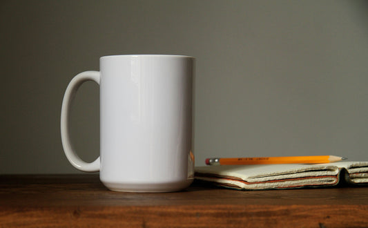 Blank white sublimation mug on a wooden desk beside a notebook and pencil, ready for pressing with the right time and temperature settings